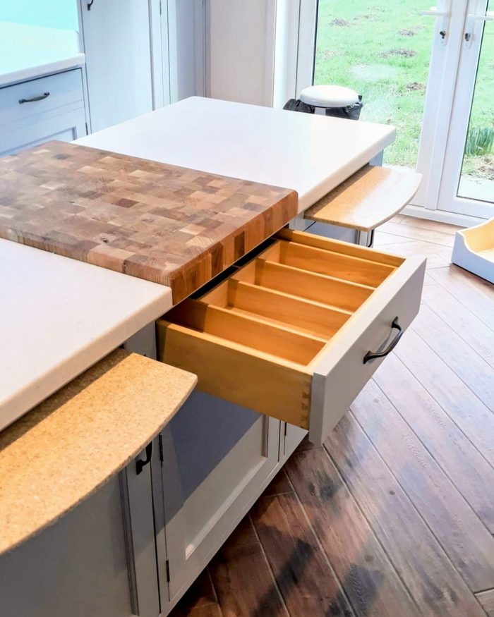 An end-grain butcher block worktop cut around a curved breakfast bar, with a fitted cutlery drawer below