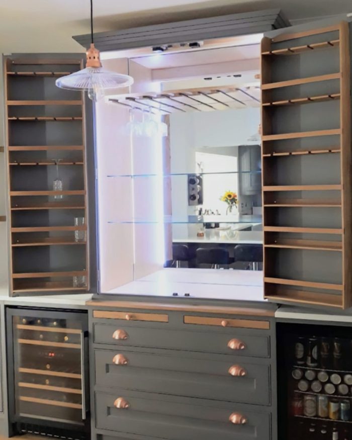 A lit drinks cabinet with racks in both doors, copper handles and a wine fridge either side