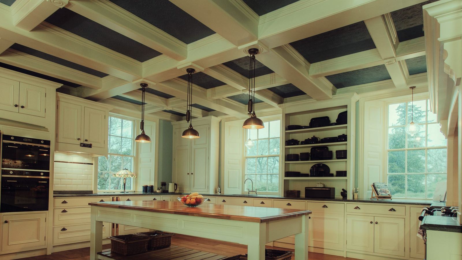 An ivory hand-painted country house kitchen with a coffered ceiling and brass pendants
