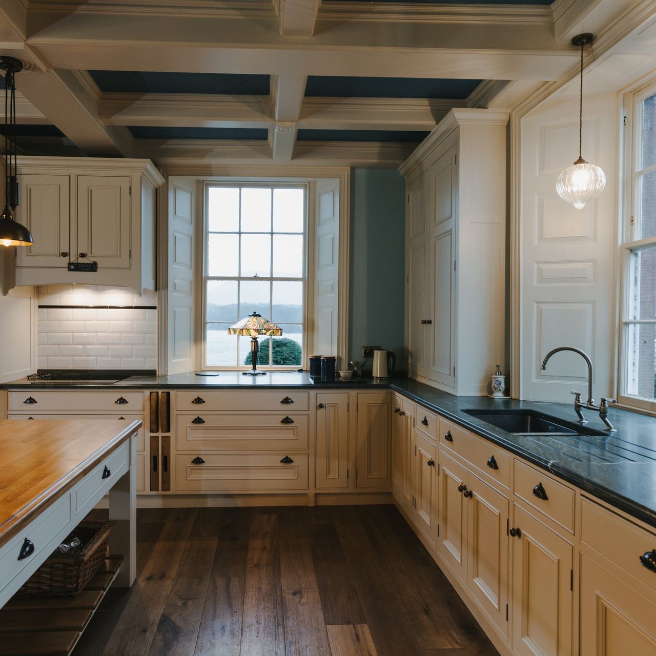 A cream in-frame kitchen looking out over a lake, with a boarded floor and a butler sink