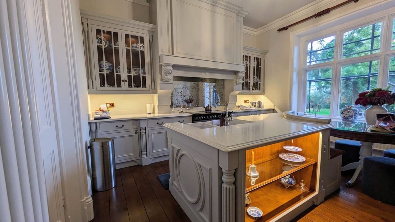 A grey painted in-frame kitchen in a vicarage, with an island and glazed dressers
