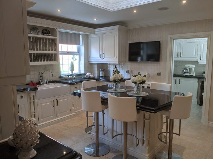 A cream painted kitchen with black granite worktops, a plate rack over a belfast sink and a breakfast bar with stools