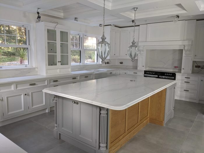 A white and grey painted kitchen with marble worktops, glass lantern pendants and a large island panelled in oak