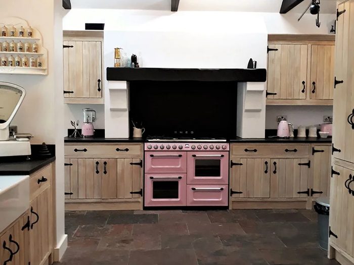 A limed oak kitchen with black iron handles, dark worktops and a pink range cooker set into a beamed chimney